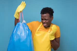 The Science of Odor Removal - man holding smelly trash bag in disgust